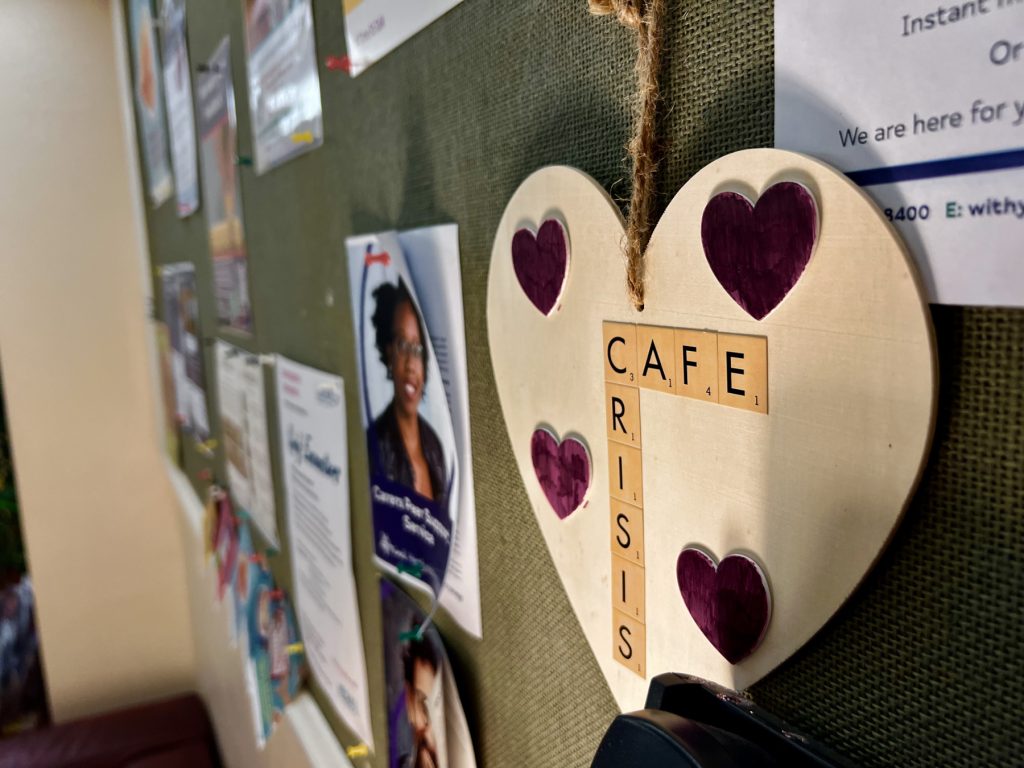 the photo shows one of the walls inside the Ware crisis cafe, featuring a wooden heart decoration with hearts and the words crisis cafe in scrabble style