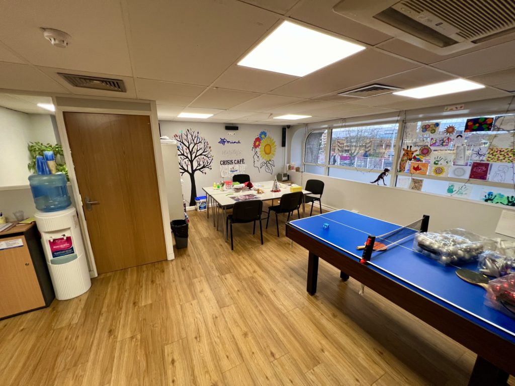 the photo shows the inside of our Stevenage Crisis Cafe, including a table football, chairs and tables, a water fountain and artwork on the walls