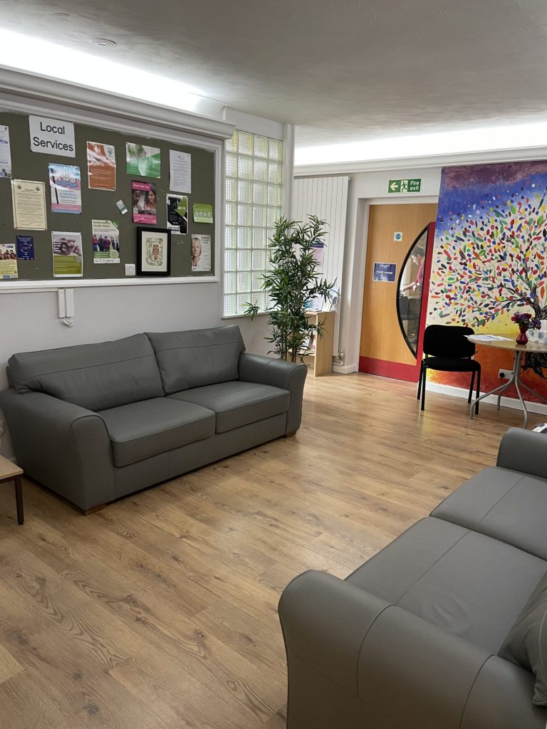 the inside of our Ware crisis cafe, which has sofas, a water machine, tables, chairs, posters, plants, and colourful artwork
